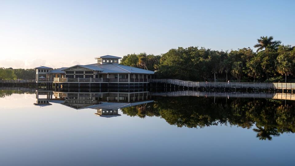 Green Cay Nature Center and Wetlands visitor pavilion in Boynton Beach, Florida reflected in calm water on clear cloudless sunny morning..