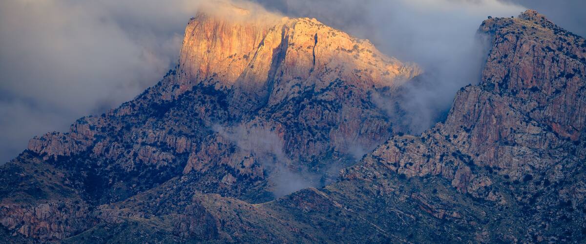 Sunlight illuminates Table Mountain in Pusch Ridge as misty storm clouds begin to clear. Tucson/Oro Valley, Arizona.