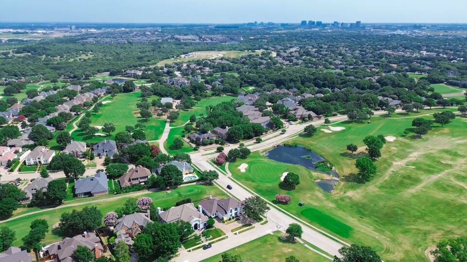 Upscale residential neighborhood urban sprawl lush greenery area with downtown Plano Texas in background, golf course community, row of two-story mansion homes swimming pool, Dallas, aerial view