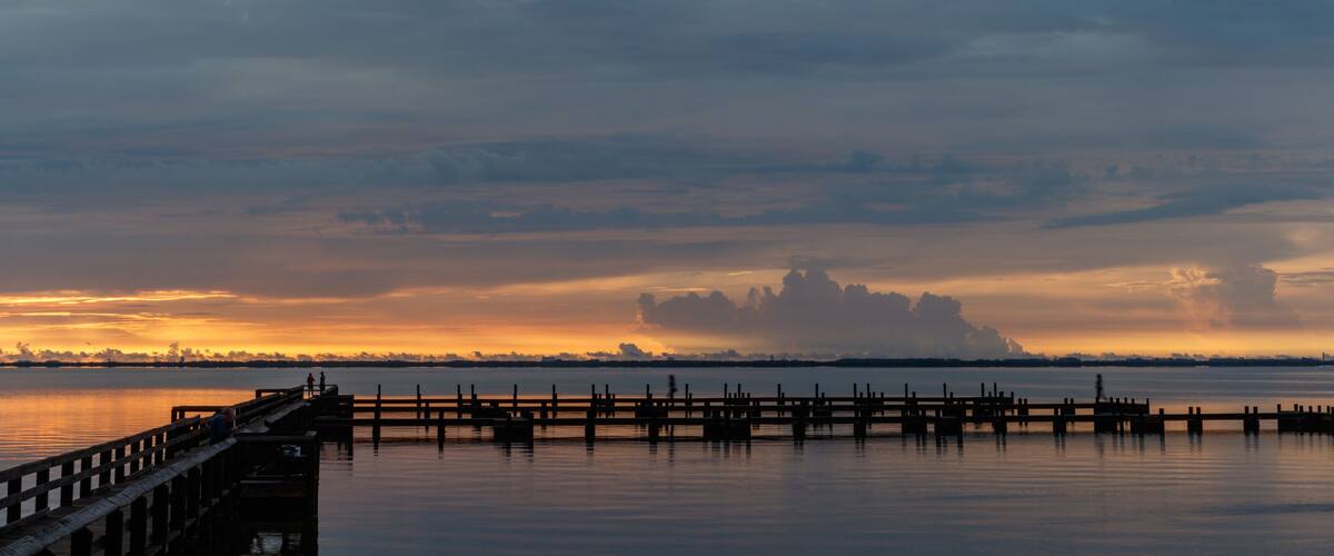 A sunset over a calm body of water with a pier extending into the water.