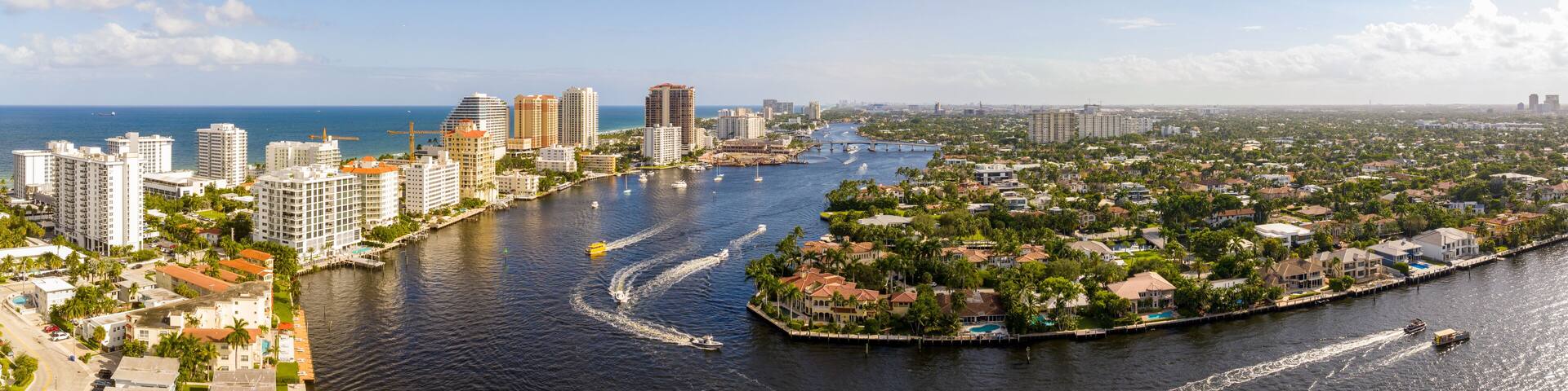 A coastal cityscape with high-rise buildings, a marina, and a river.