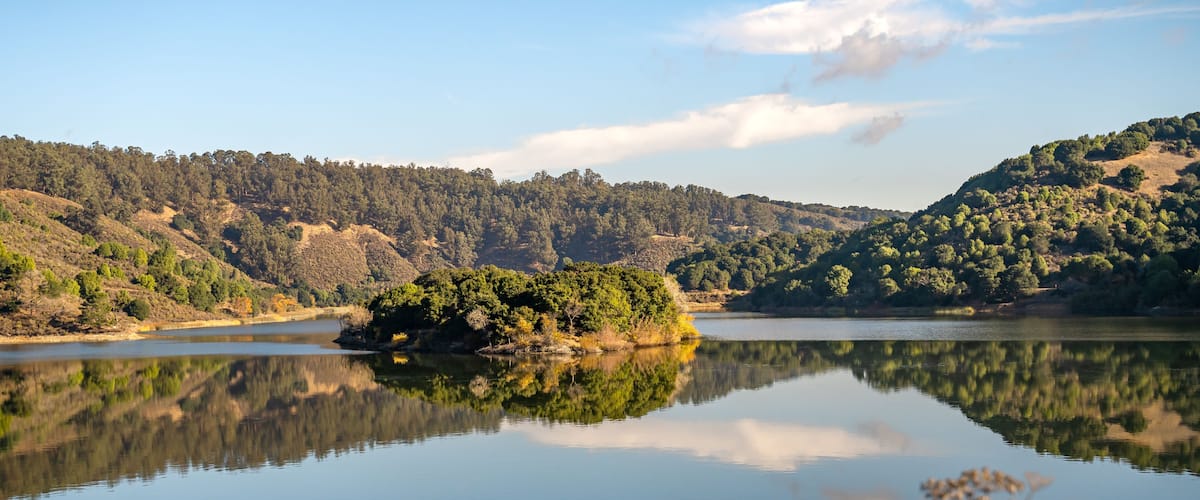 A calm lake with a small island in the center, surrounded by forested hills.