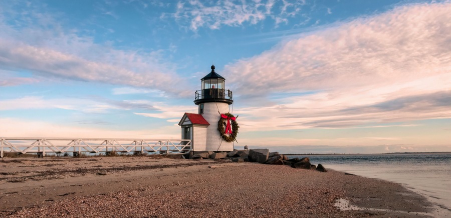 Un faro con techo rojo y un adorno, un muelle blanco y una playa de piedras.