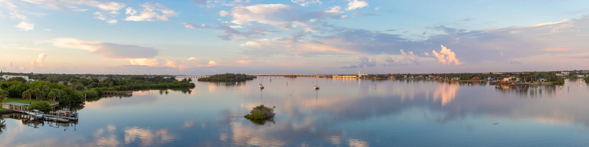 A calm lake with boats, a dock, and a distant city skyline under a partly cloudy sky.