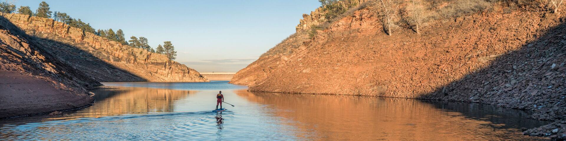 Silhouette of a stand up paddler on a mountain lake in winter scenery - Horsetooth Reservoir in northern Colorado, fitness and recreation concept, panoramic web banner