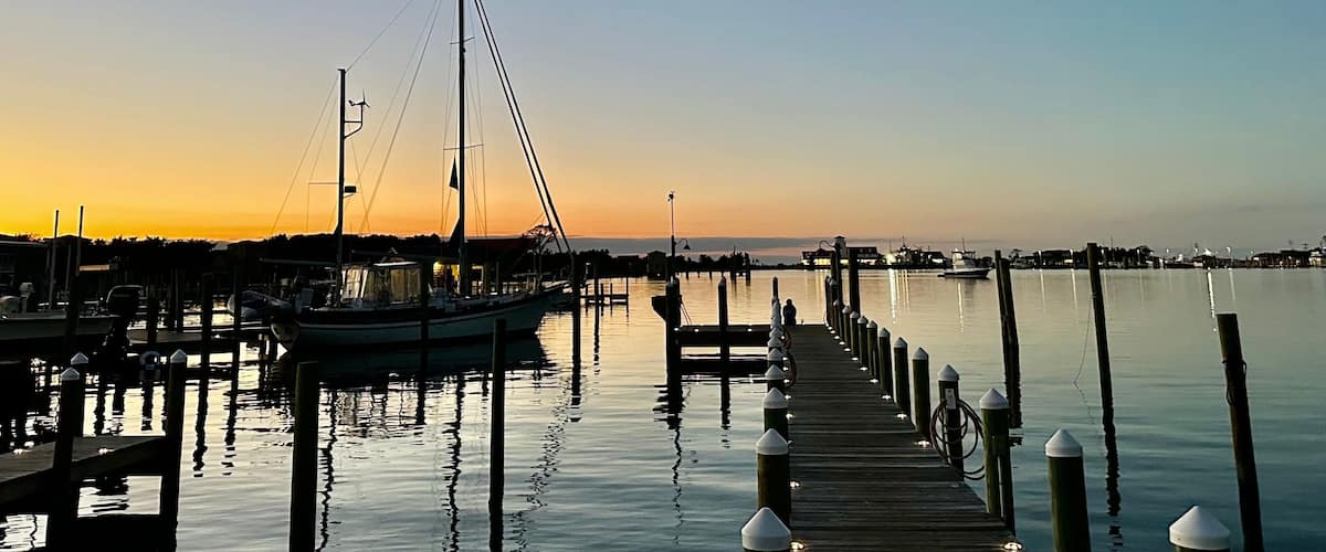 Boats moored in Silver Lake Harbor at sunset, with a pier extending into the calm water, under a gradient evening sky in Ocracoke, North Carolina.