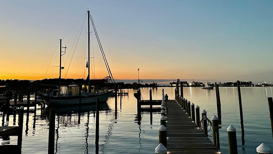 Boats moored in Silver Lake Harbor at sunset, with a pier extending into the calm water, under a gradient evening sky in Ocracoke, North Carolina.
