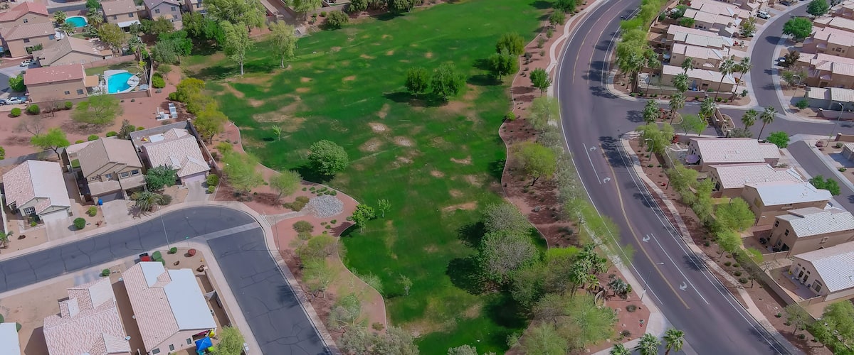 An aerial view of a residential area with houses, roads, and a large green field.