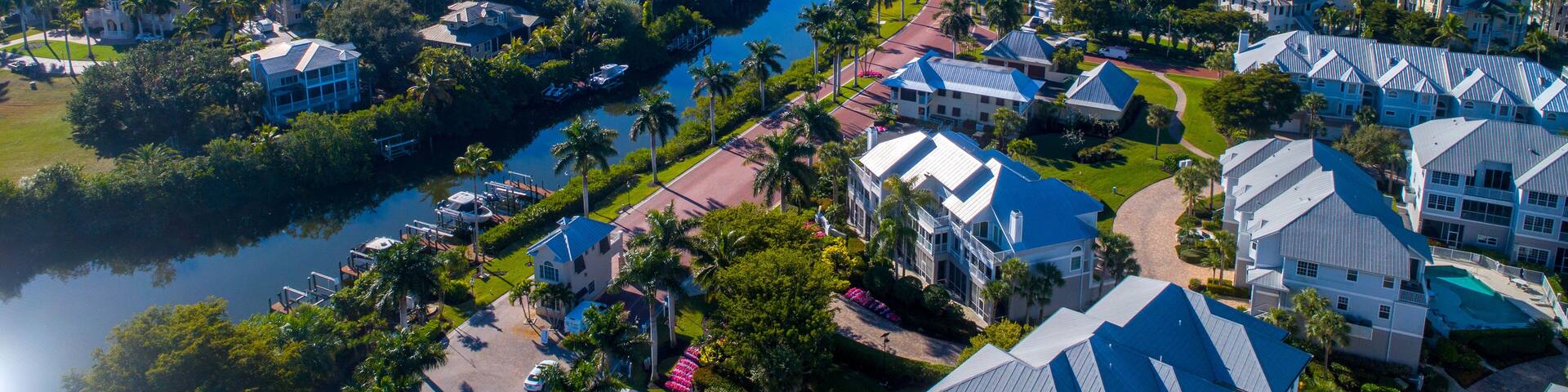 Aerial Perspective from Drone Featuring the Barefoot Beach in Bonita Springs, Florida. Blue Water Coastline with Clear Sky and Wispy Clouds in the Background and Clusters of Homes in the Foreground