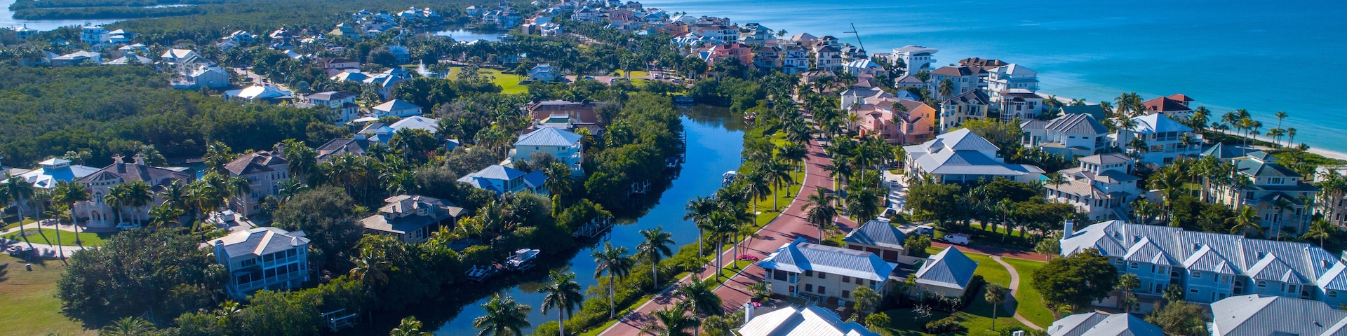 Aerial Perspective from Drone Featuring the Barefoot Beach in Bonita Springs, Florida. Blue Water Coastline with Clear Sky and Wispy Clouds in the Background and Clusters of Homes in the Foreground