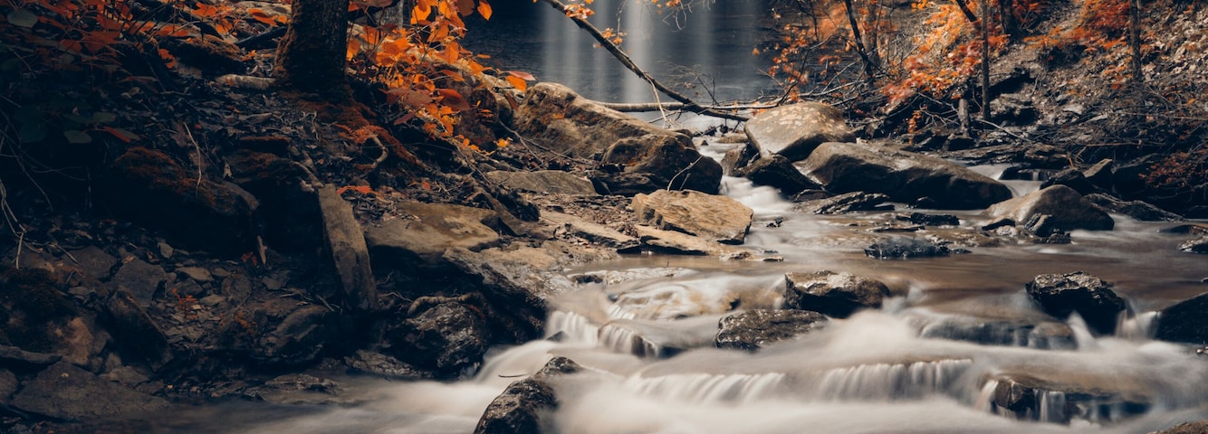 Bridal veil falls waterfall from Heber Springs during peak autumn color with orange fall leaves decorating the streaming water cascade though the rocks.