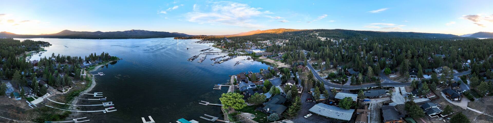 A panoramic view of a lake surrounded by dense forests and a small town with docks and boats.