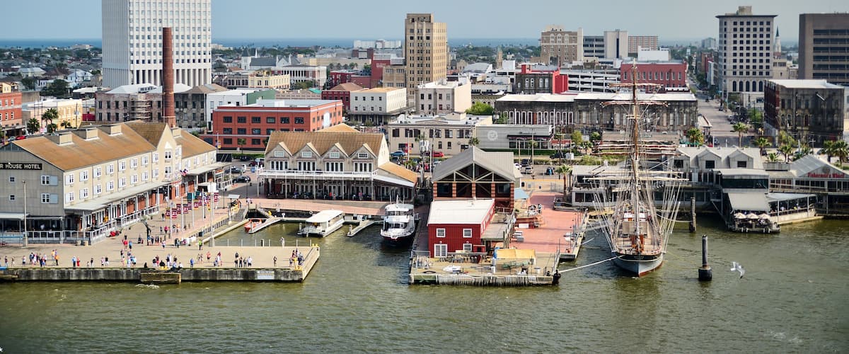 A waterfront cityscape with a tall modern skyscraper, historic buildings, and a dock with boats.