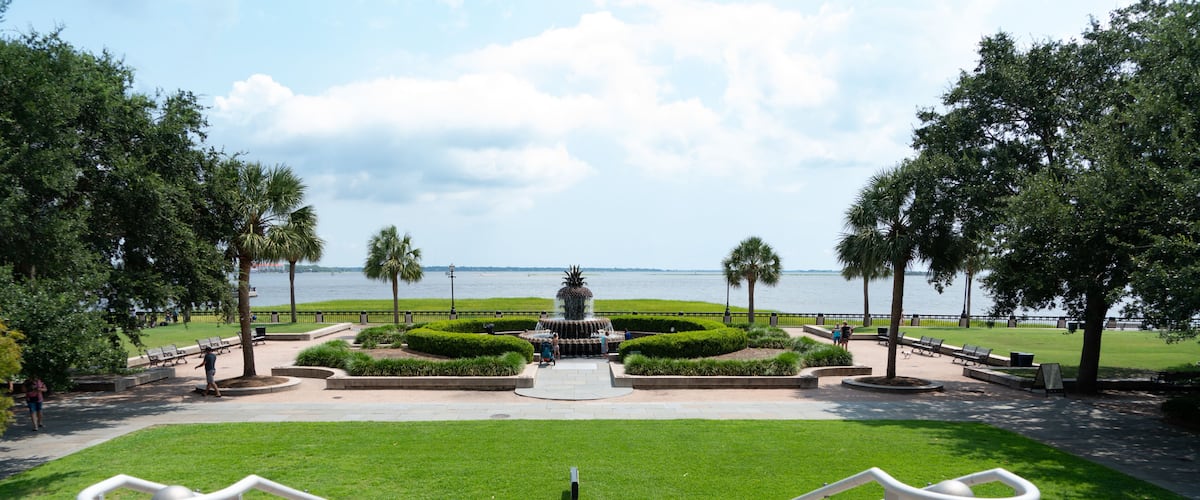 A park with a fountain, a view of the water, and a staircase leading to the fountain.