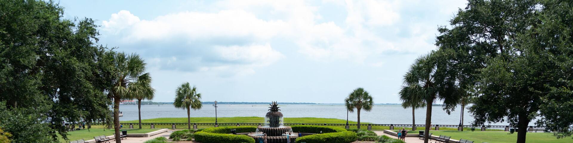 A park with a fountain, a view of the water, and a staircase leading to the fountain.