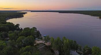 A large body of water surrounded by dense forest and a few buildings.
