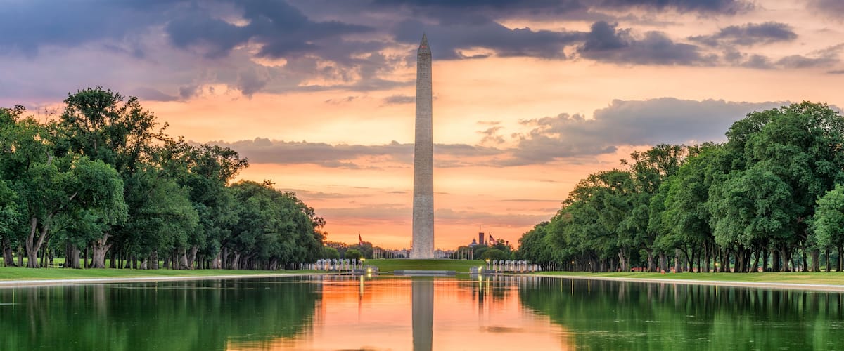 El Monumento a Washington reflejado en aguas tranquilas, rodeado de árboles y un cielo al atardecer.