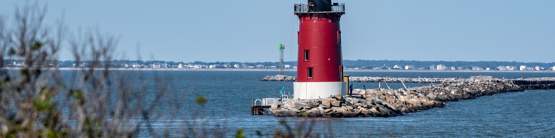 Un phare rouge et blanc, perché sur un promontoire rocheux, avec une étendue d’eau calme au premier plan et un ciel dégagé.