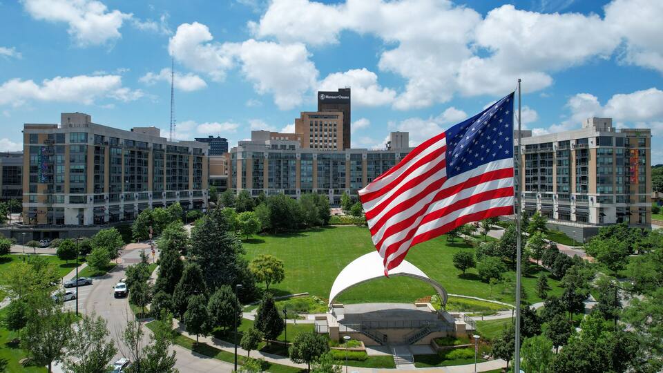 A large American flag in front of a modern building complex with multiple high-rise structures.
