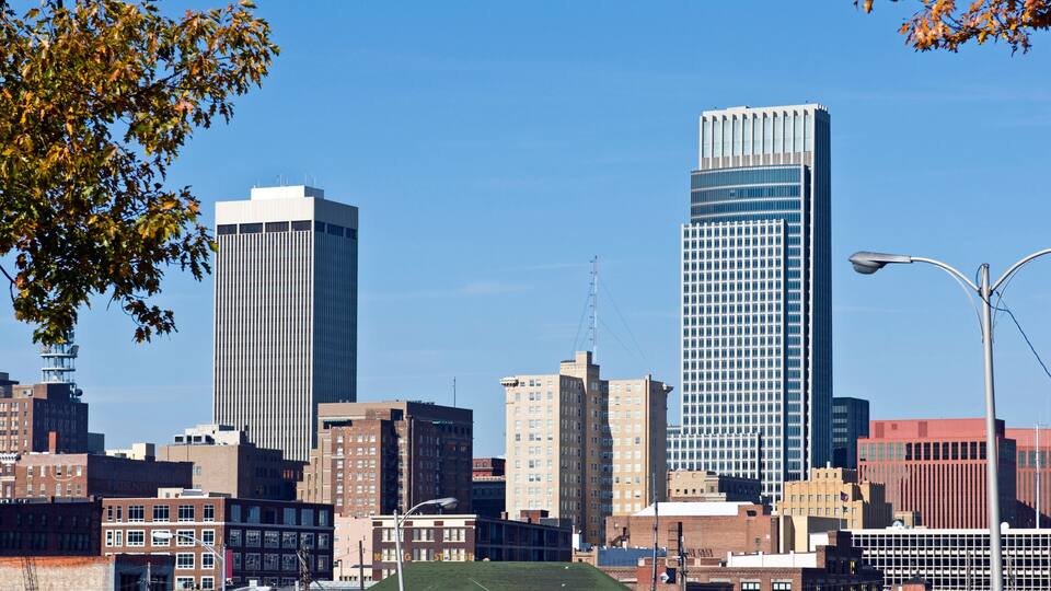 A city skyline with tall buildings, including a prominent skyscraper with a grid-like facade and a shorter building with vertical lines.