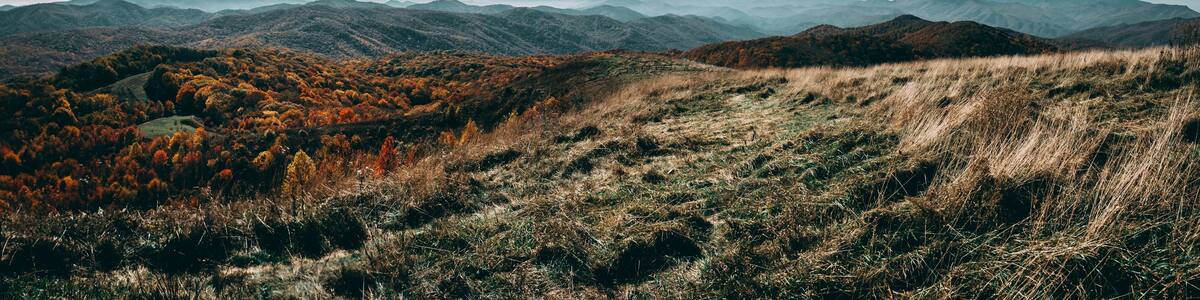 A mountainous landscape with autumn foliage and distant mountain ranges under a cloudy sky.