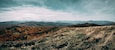 A mountainous landscape with autumn foliage and distant mountain ranges under a cloudy sky.