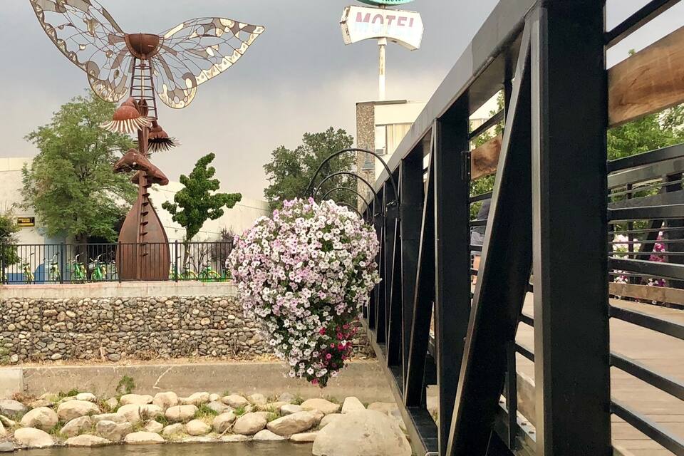 A bridge with a metal railing, a decorative metal sculpture, a stone wall, and a sign for "Reno Riviera Motel".