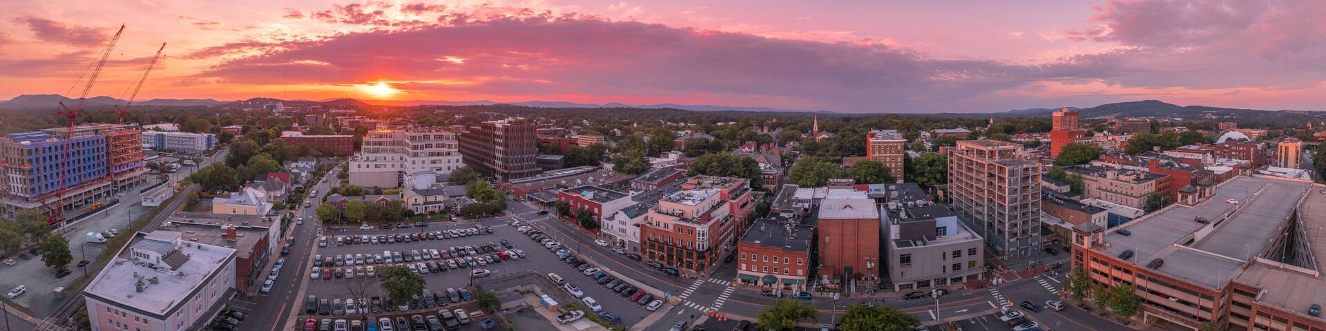 Aerial sunset view of downtown Charlottesville, Virginia with new construction office apartment building, city market parking lot, parking garage and the mall with dramatic colorful purple orange sky