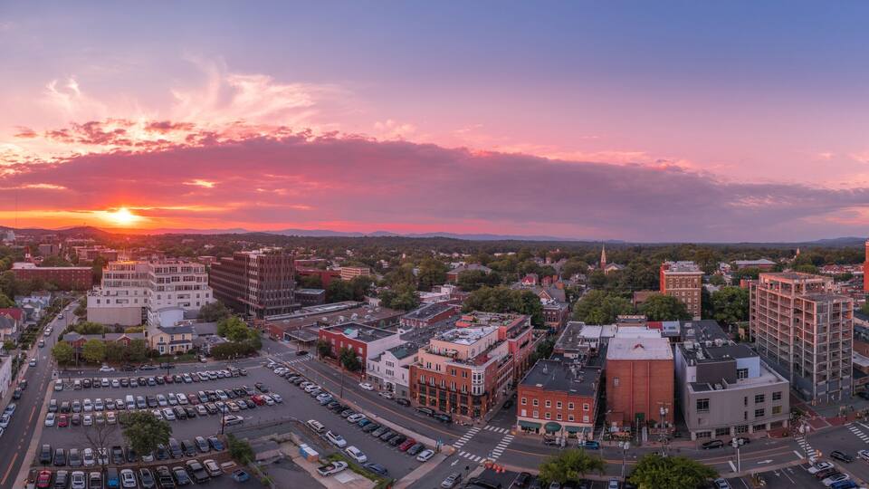 Aerial sunset view of downtown Charlottesville, Virginia with new construction office apartment building, city market parking lot, parking garage and the mall with dramatic colorful purple orange sky