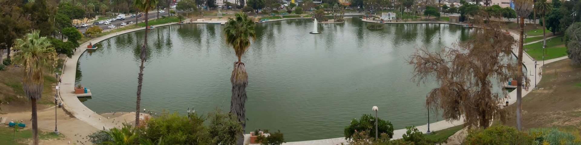 Macarthur Park in Los Angeles, California, USA. A scenic view of the park's lake and the city skyline. People are enjoying the park's amenities, walking, and relaxing.