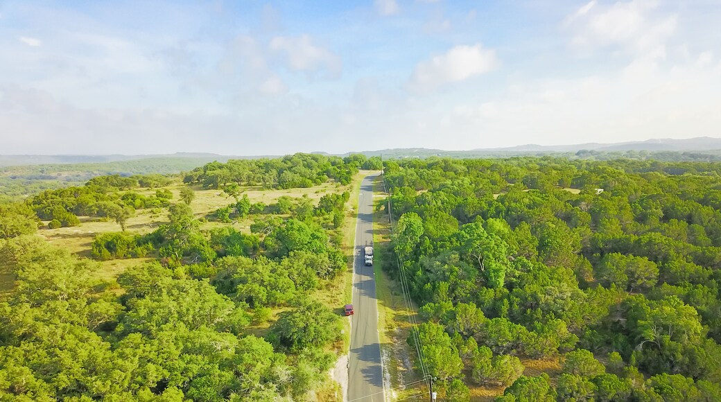 Top view scenic winding country road through green farmland in Hill Country. Aerial rural road though countryside of Texas ranch, blue sky