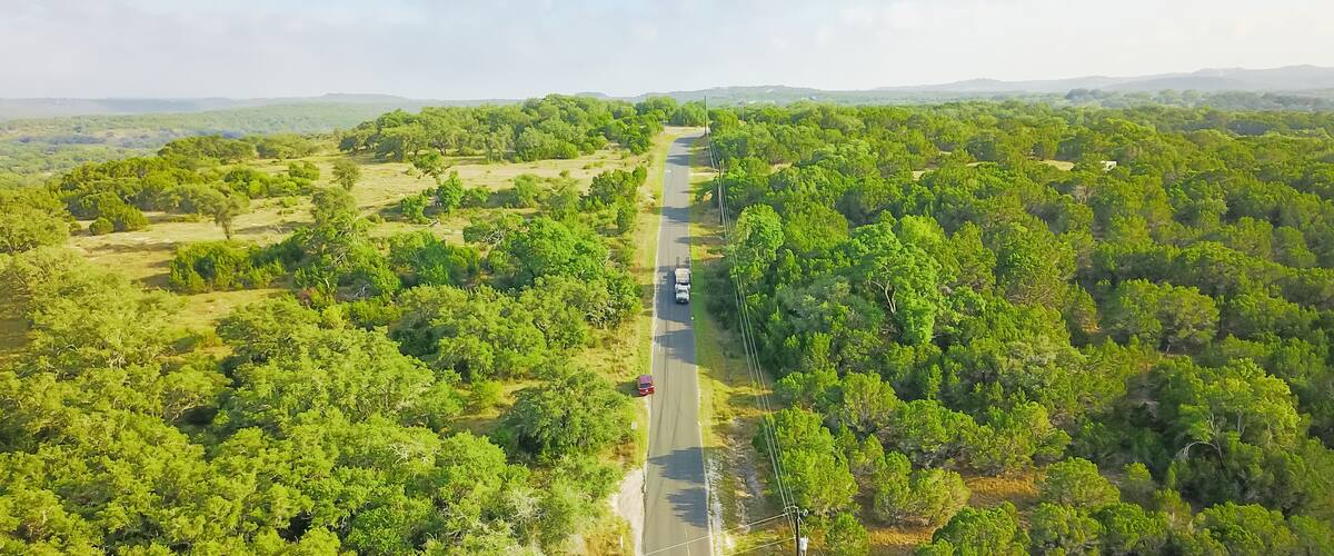 Top view scenic winding country road through green farmland in Hill Country. Aerial rural road though countryside of Texas ranch, blue sky