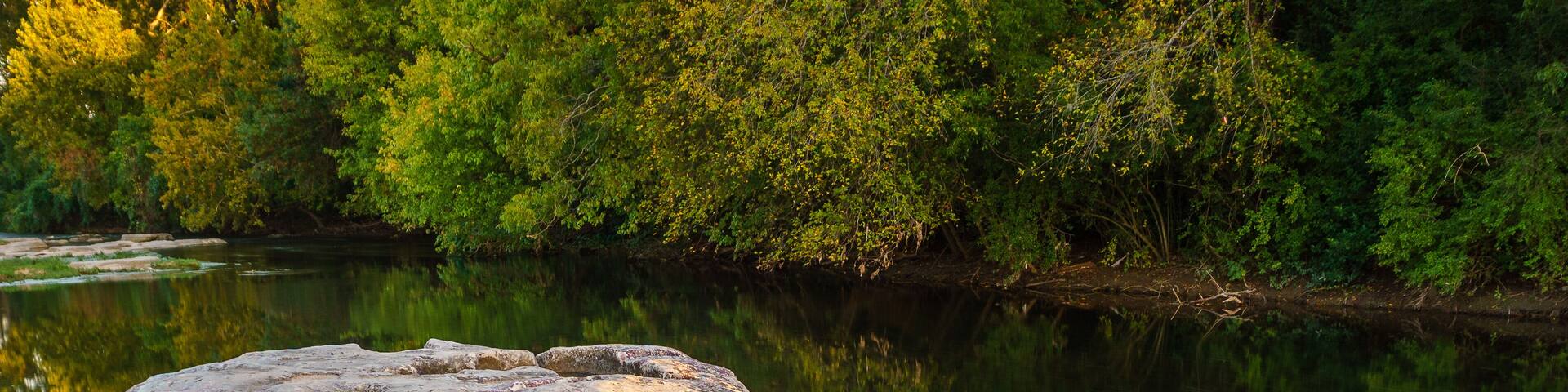 A large rock formation surrounded by calm water and dense green foliage.