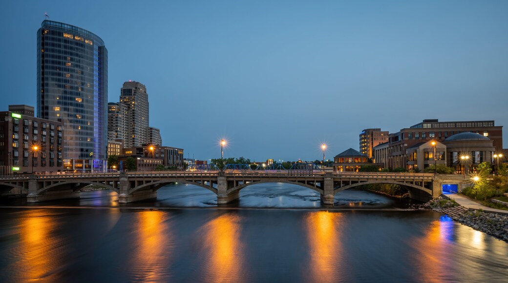 A cityscape at dusk with a river, a bridge, and modern buildings.