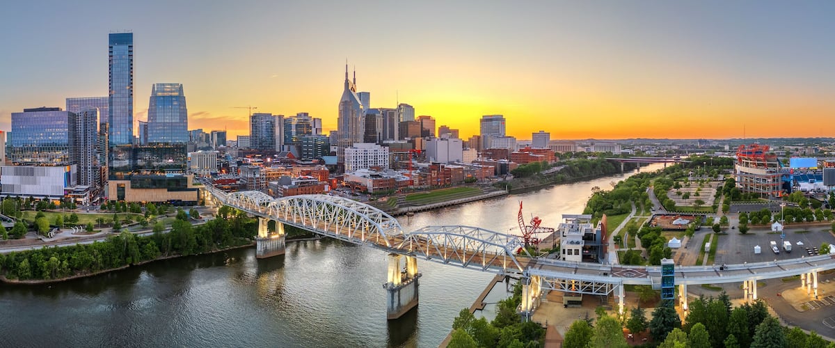 A city skyline at sunset with a prominent bridge over a river.