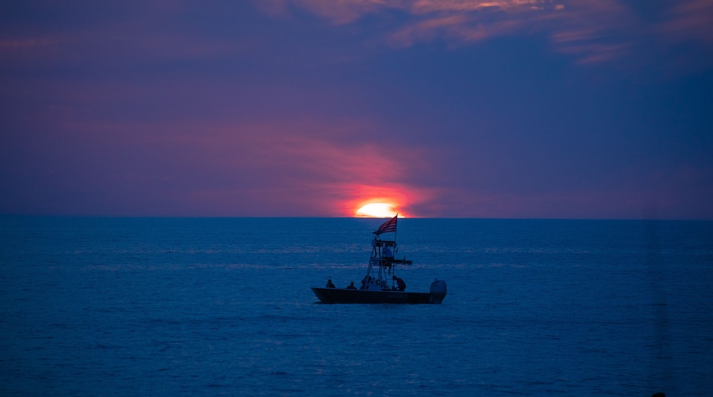 A boat on the blue ocean water in front of a glowing setting sun amid the blue and purple clouds of evening, as seen from a beach on the Gulf of Mexico near Englewood, Florida, USA, in early spring