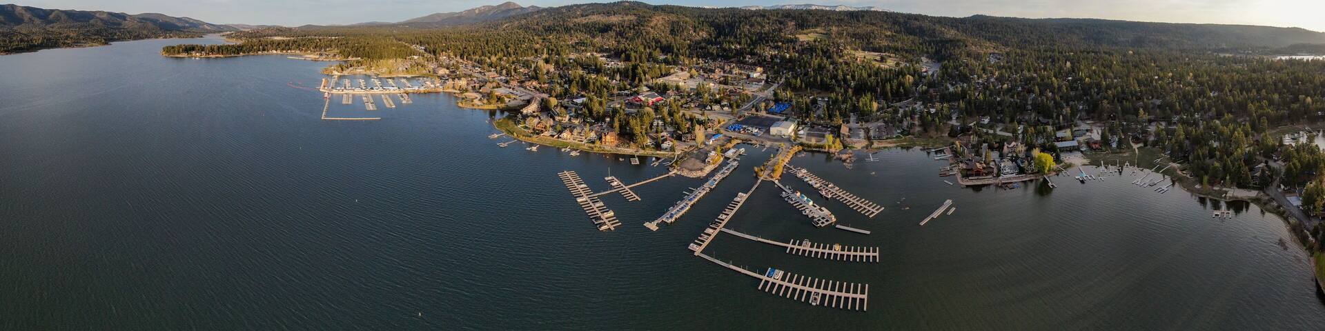 An aerial view of a lakeside community with docks, a marina, and surrounding forested hills.