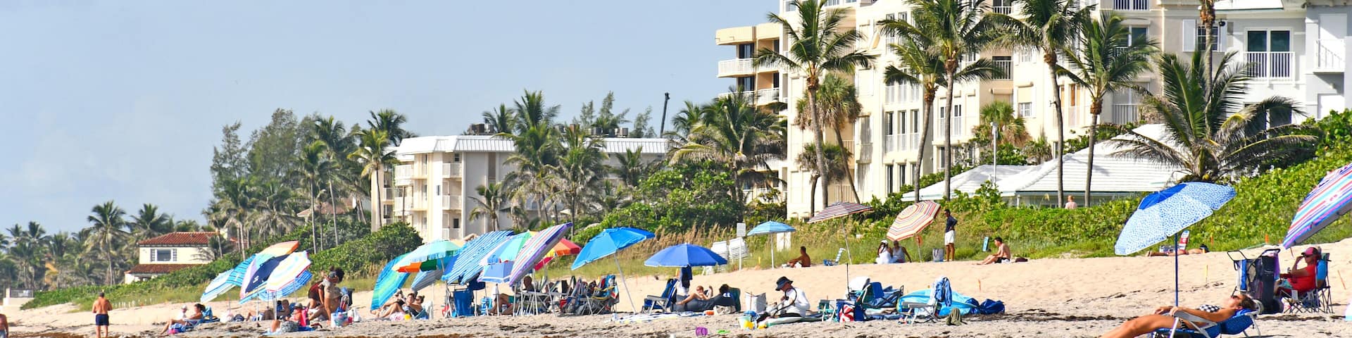 Tourists and locals with umbrellas on the beach with condos in the background at Lantana Beach in South Florida