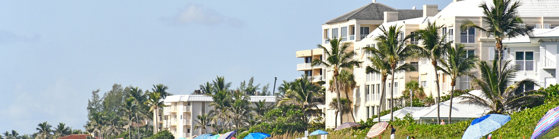 Tourists and locals with umbrellas on the beach with condos in the background at Lantana Beach in South Florida