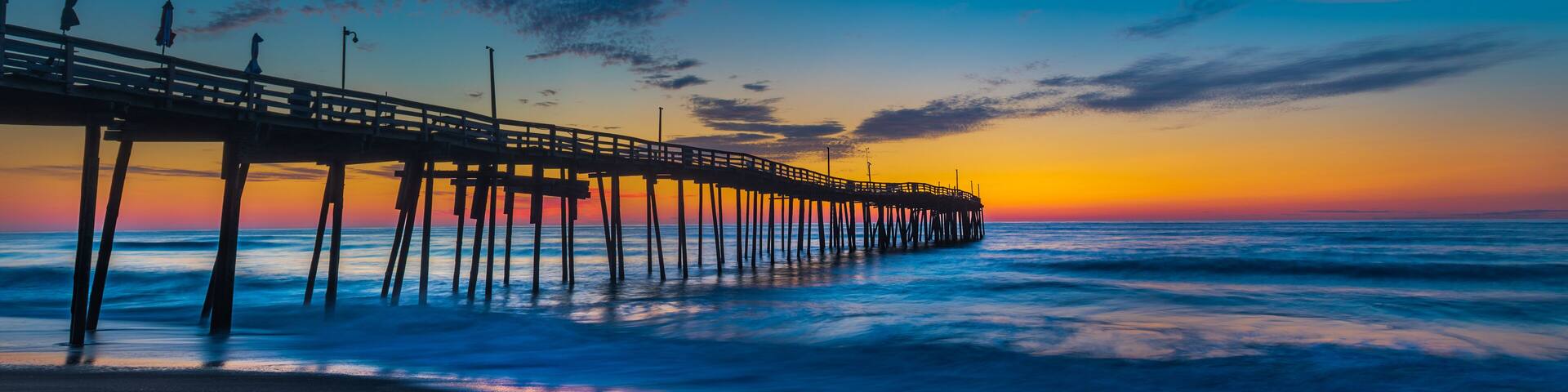 A pier extending into the ocean at sunset with a clear sky and calm sea.