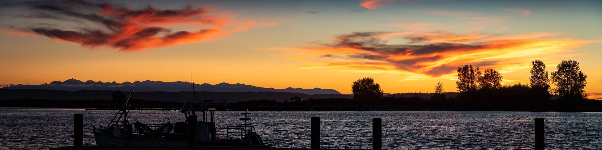 A sunset over a body of water with mountains in the background and a dock with a boat.