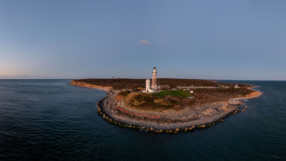 Vue aérienne d’un phare situé sur une île rocheuse, entouré d’une mer calme.