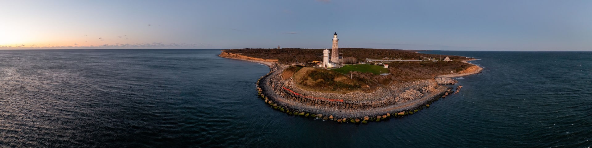 An aerial view of a lighthouse on a rocky island surrounded by calm sea.