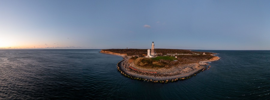Vue aérienne d’un phare situé sur une île rocheuse, entouré d’une mer calme.