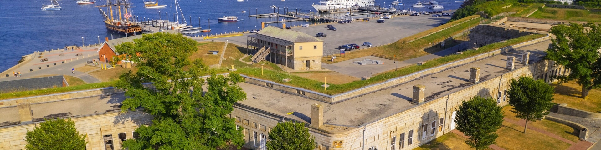 A coastal harbor with numerous sailboats and a historic building with a flat roof.