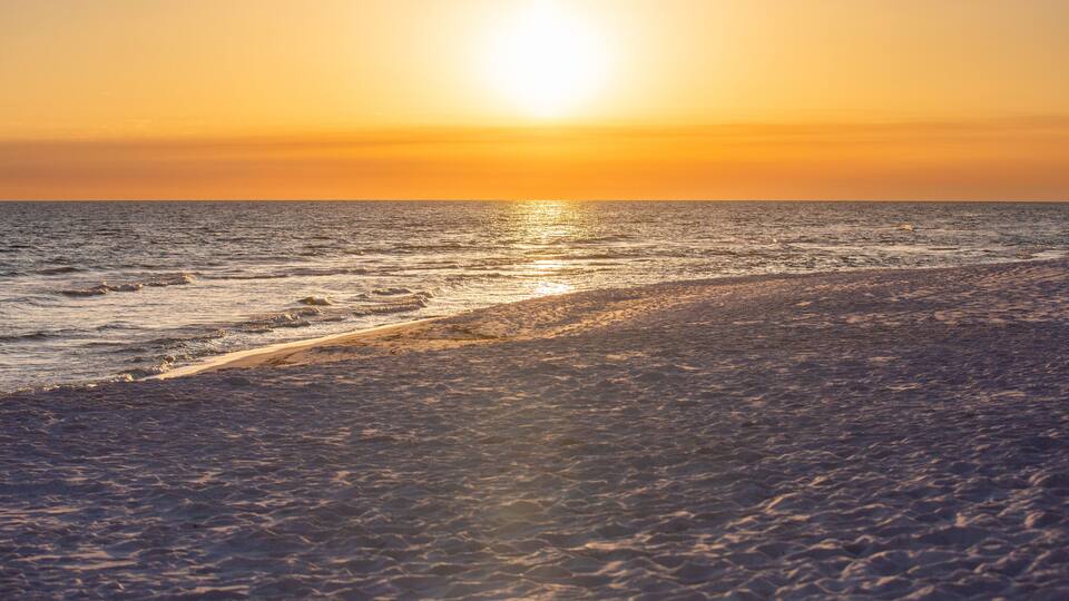 Ein Strand bei Sonnenuntergang mit Wellen und bewölktem Himmel.