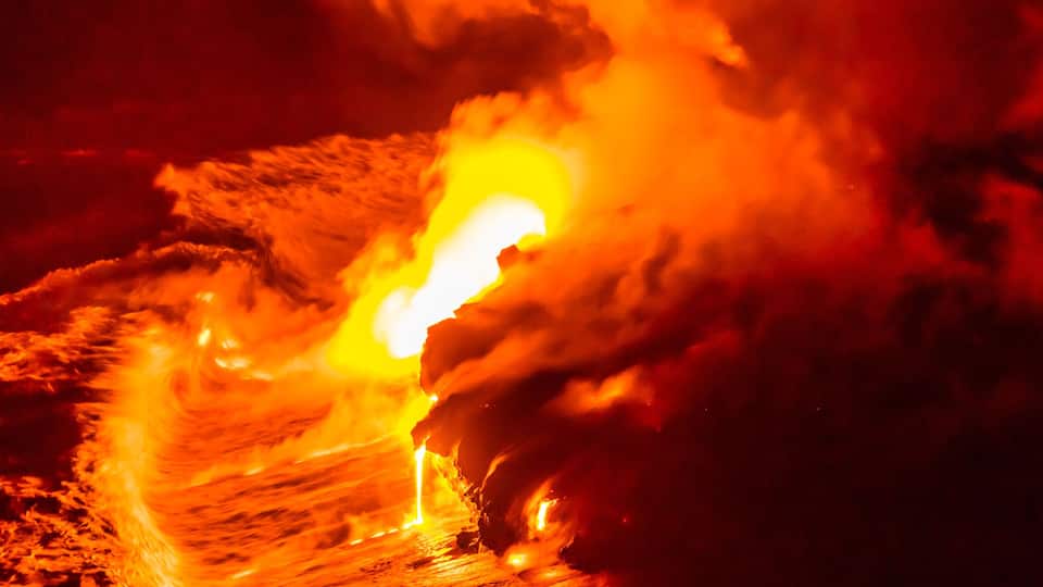 Lava flow falling in ocean waves in Hawaii from Hawaiian Kilauea volcano at night. Molten lava washed by the sea water crashing in, Big Island, USA.