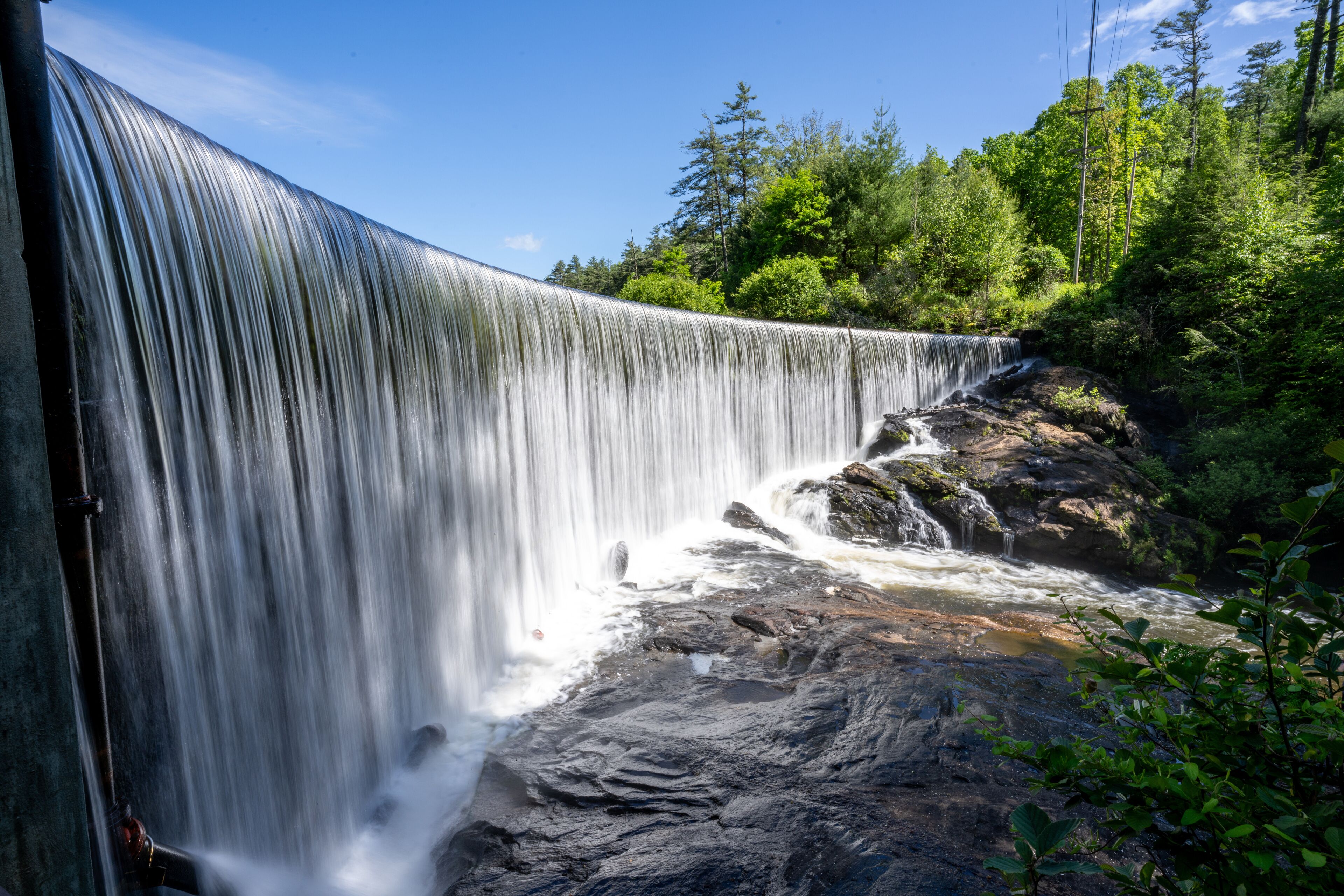 A curved curtain of water flowing over the perfectly level dam that forms Lake Sequoyah blocking the Cullasaja River, Highlands, North Carolina