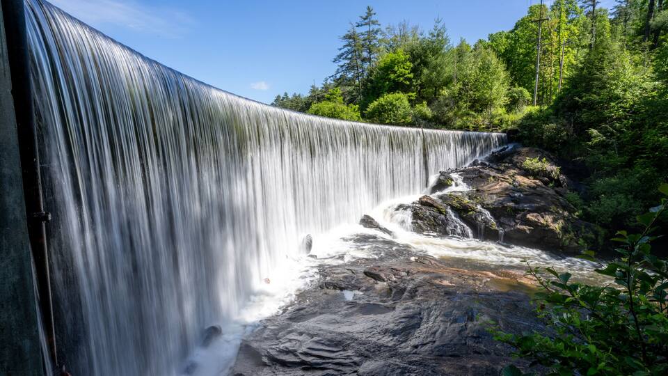A curved curtain of water flowing over the perfectly level dam that forms Lake Sequoyah blocking the Cullasaja River, Highlands, North Carolina