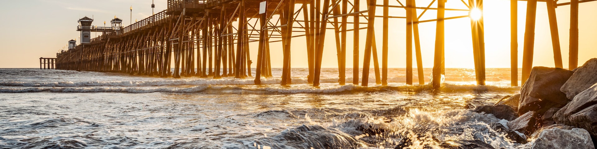 Une jetée qui s’avance dans l’océan, avec des vagues qui se brisent contre les rochers au coucher du soleil.